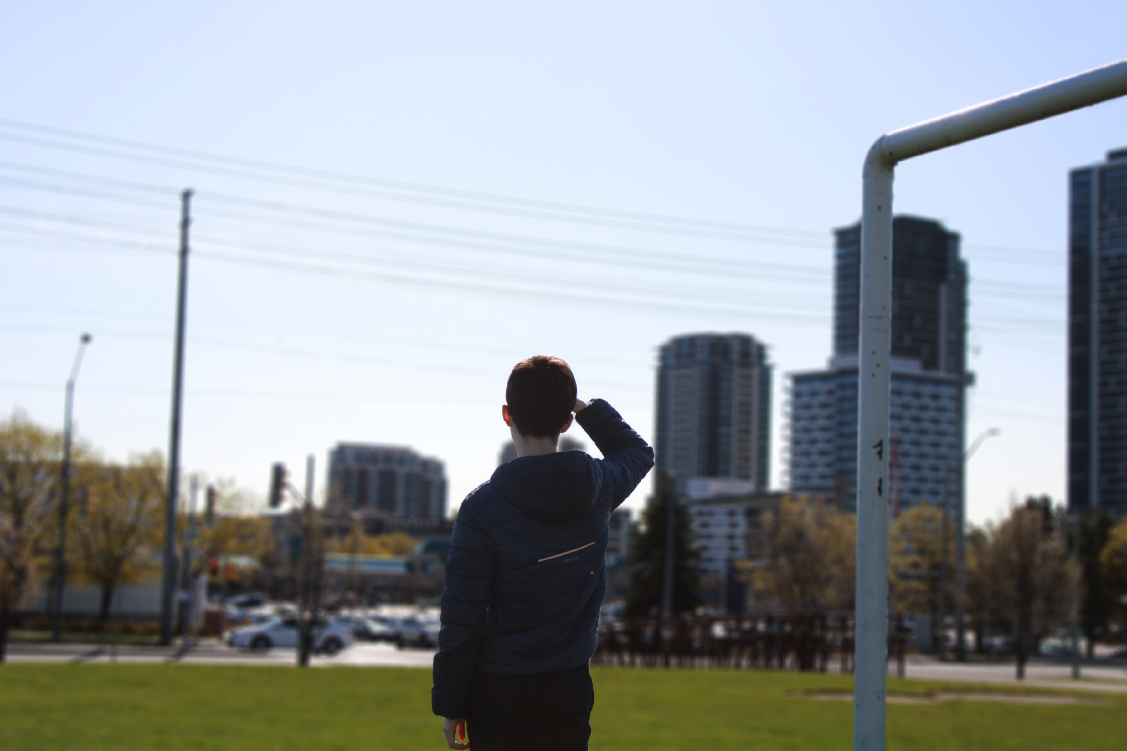 A guy standing in a field, staring off to the plaza across the street from him