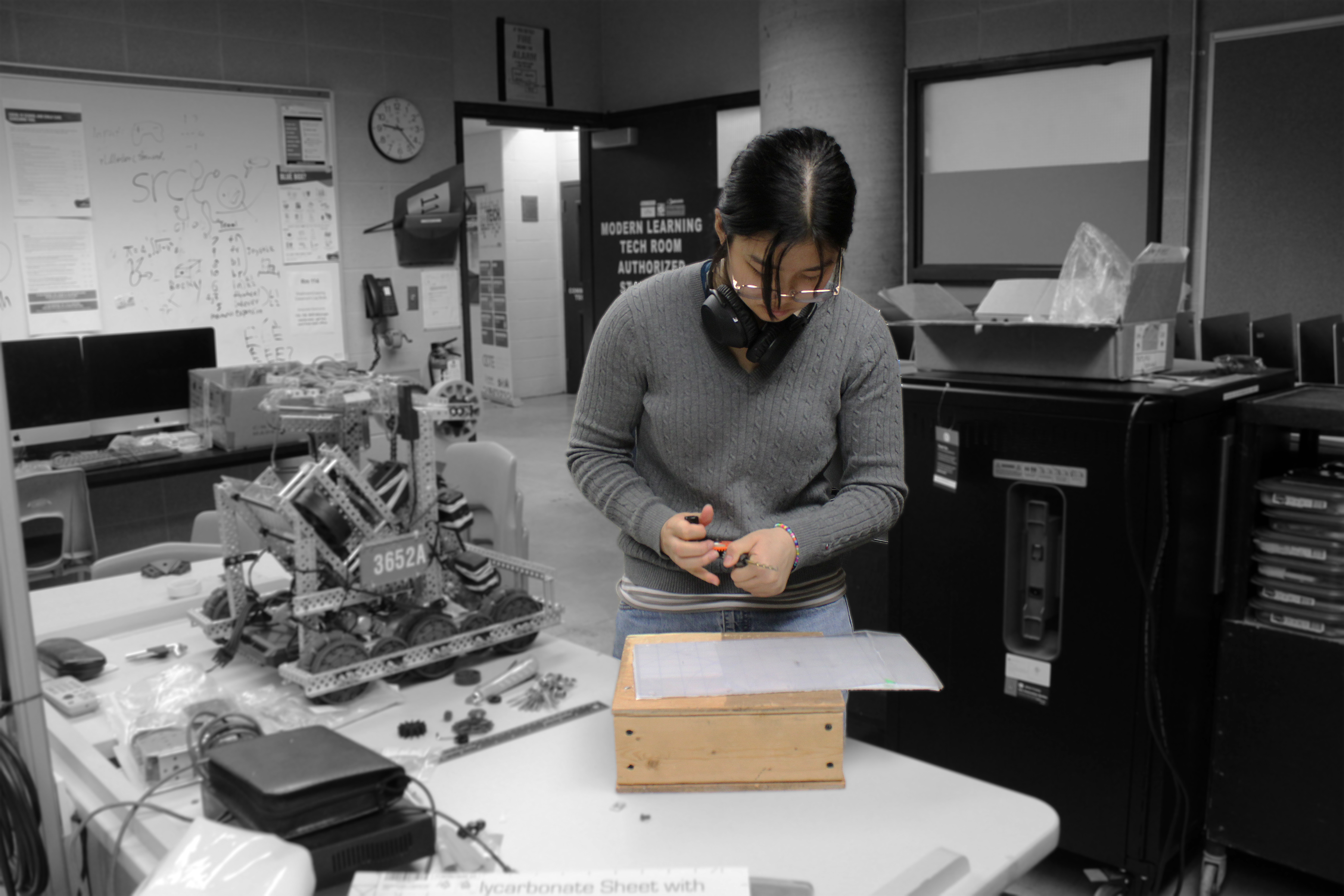 A gal drilling into a piece of plastic (for robotics)