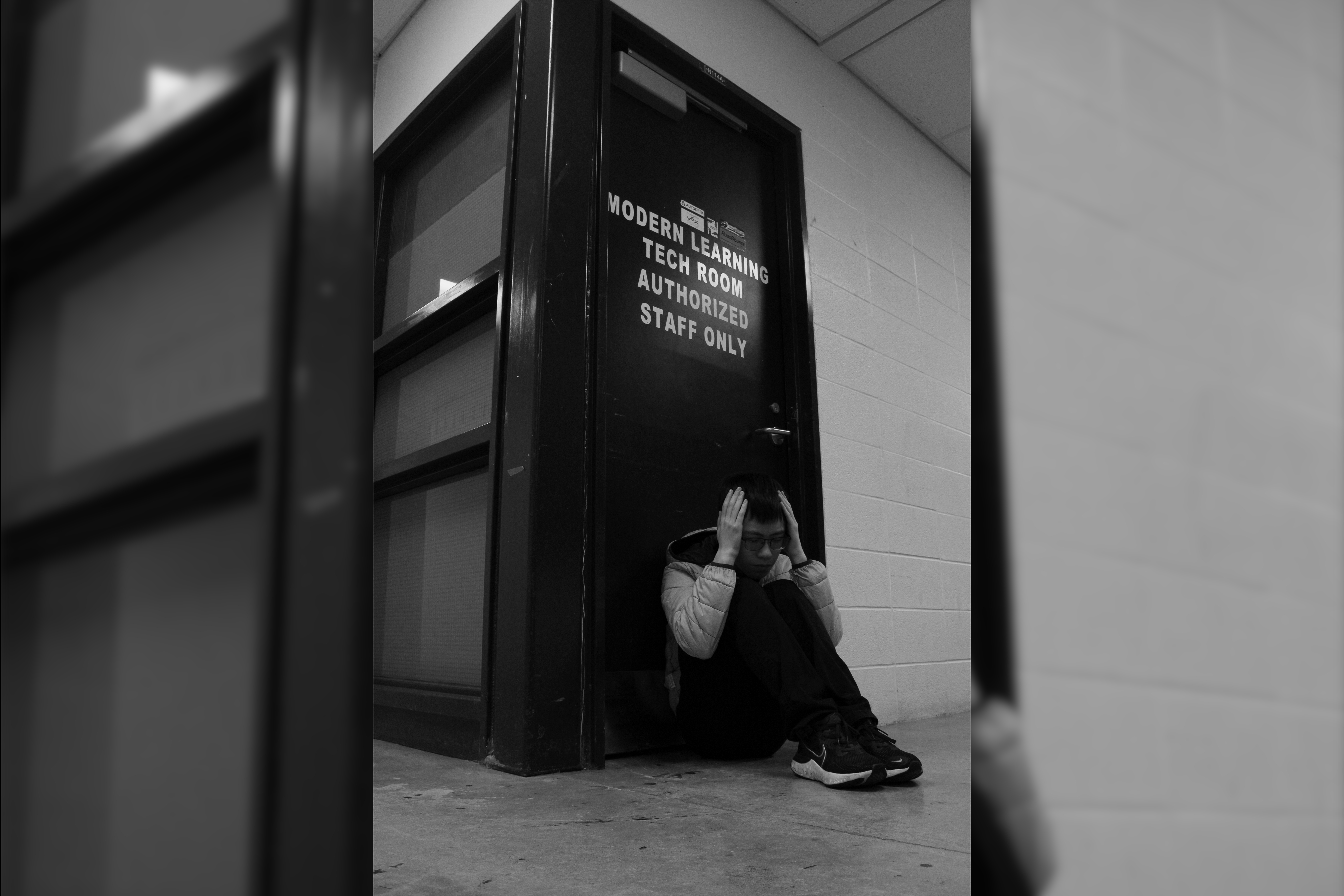 Wide shot of a guy hunched over in anguish, sitting at a door