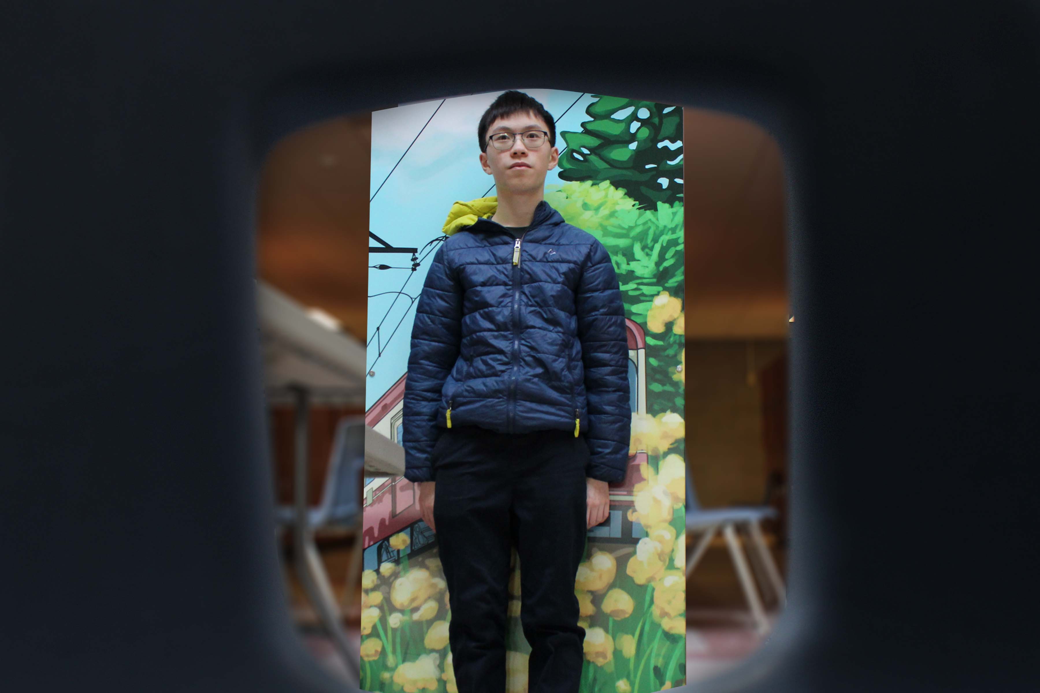 A guy standing in front of a row of lockers, framed by the hole in a school chair